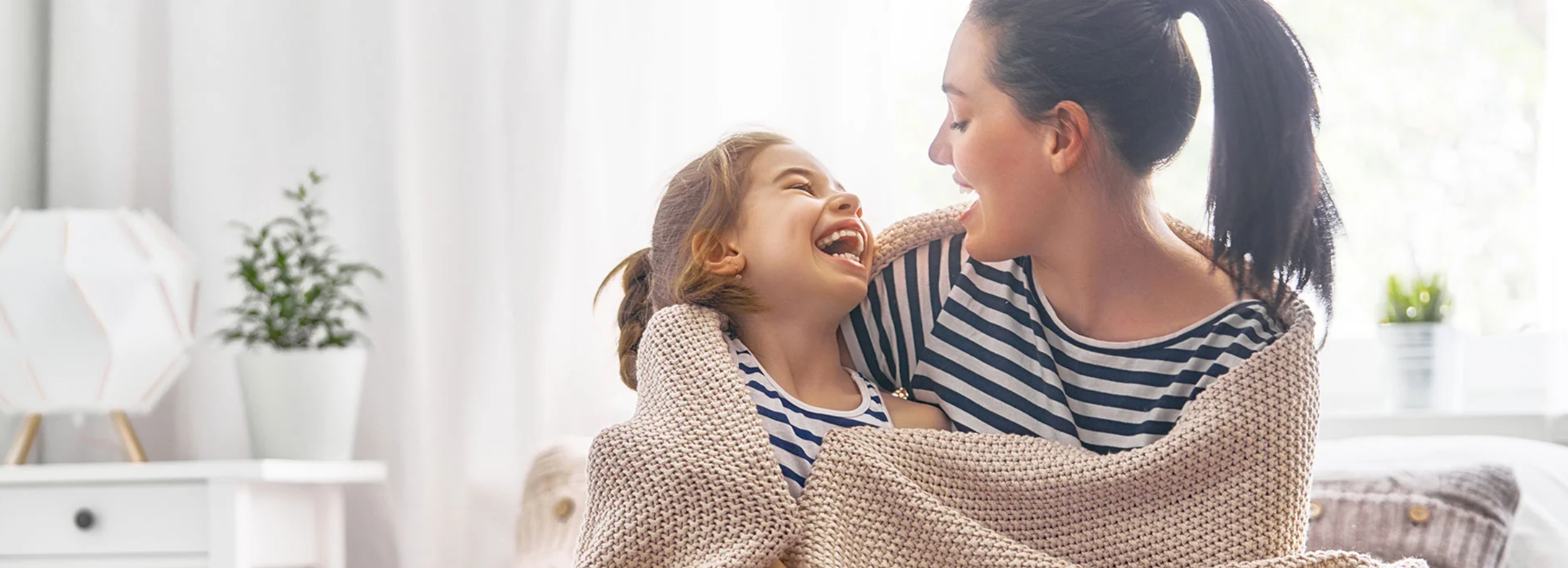 Mother and daughter laughing while wrapped in a knit blanket.