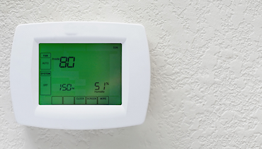 Programmable thermostat with green touchscreen on ivory stucco wall.