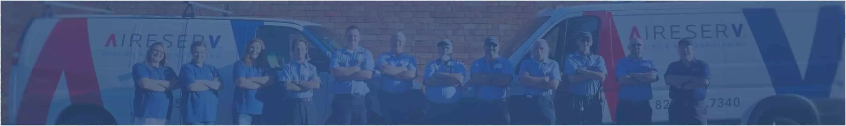 Row of Aire Serv technicians with their arms crossed standing in front of an Aire Serv work van and brick wall. 