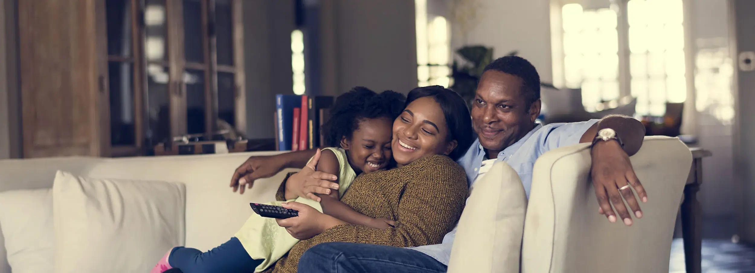 African American family or three smiling and hugging on living room sofa.