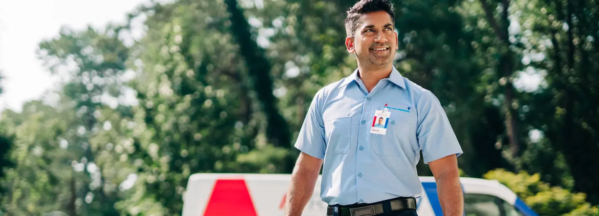Smiling South Asian male Aire Serv technician in branded blue collared shirt arriving for residential service call.