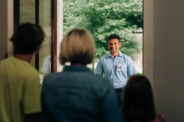 Smiling male technician greeted by family silhouetted against doorway.