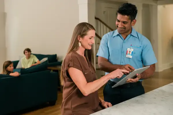 Customer and technician pointing at tablet device beside pair of children sitting in living room background.