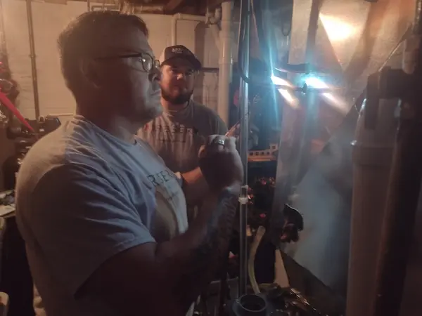 Pewaukee, WI, HVAC technicians fixing furnace unit in basement.