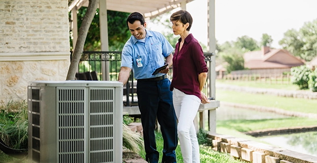 An Aire Serv technician talks with a customer by their air conditioning unit outside.