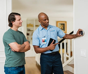 Aire Serv tech showing thermostat to customer.