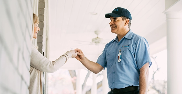 Aire Serv tech handing card to female customer at front door.