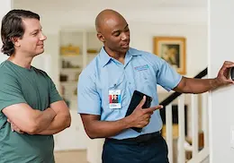 Aire Serv technician explaining thermostat settings to a homeowner inside a residence.