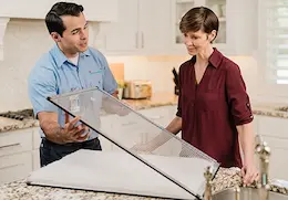 Aire Serv technician showing a homeowner a clean air filter in a kitchen.