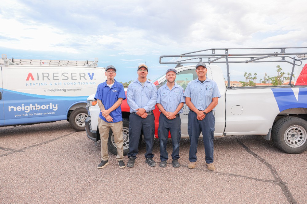 Four Aire Serv of East Valley Technicians posing together in front of an Aire Serv van and truck