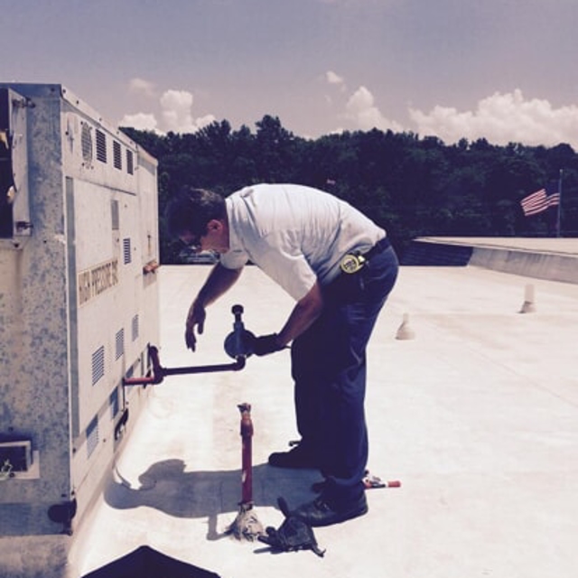 HVAC technician on a rooftop working on a unit while holding a section of piping