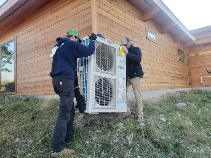Two Aire Serv of Kalispell technicians installing a heat pump unit on the side of a home.