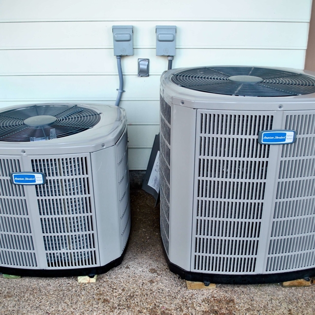 Two brand-new air conditioner condenser units installed outdoors for residential cooling.
