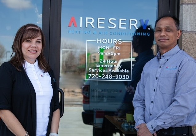 Aire Serv of Front Range technician standing next to a door displaying the company logo and business hours.