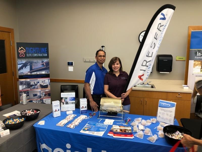 Owner of Aire Serv of Front Range at a home show booth with a table full of giveaways.