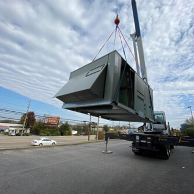 Large new HVAC system being lifted by a crane onto a building