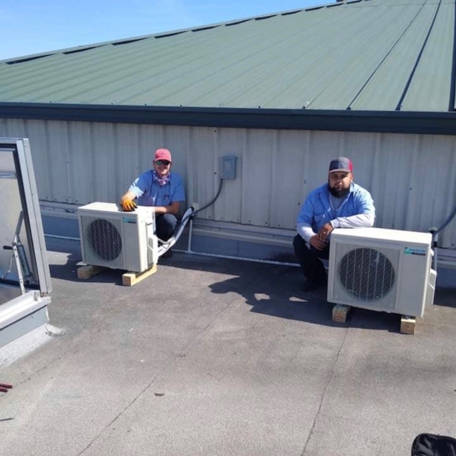 Two HVAC technicians on a rooftop squatting next to outdoor mini-split units