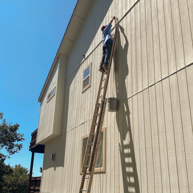 HVAC technician on a ladder working high on a home exterior