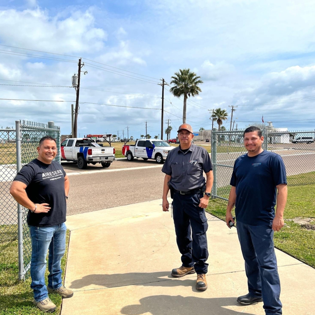Three HVAC Technicians Standing Outside With Two Aire Serv Trucks In Background