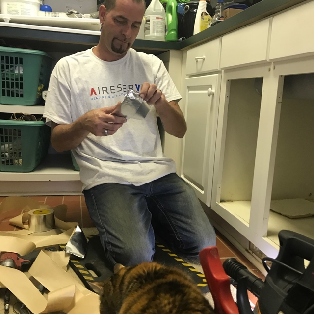 HVAC technician working under a cabinet, holding ductwork tape