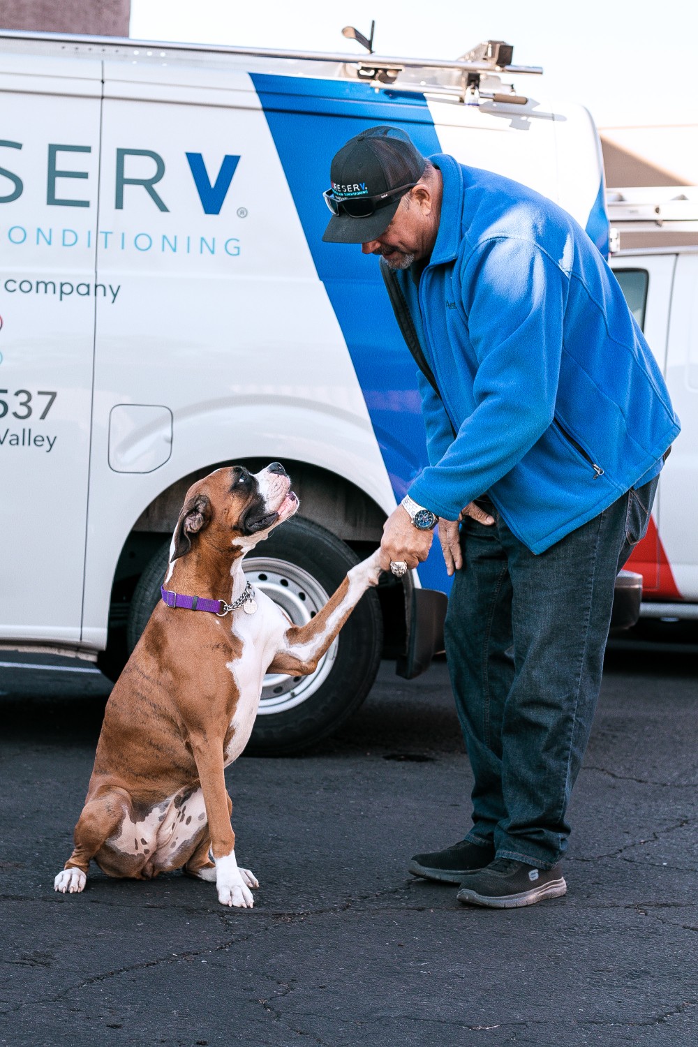 Aire Serv technician standing in front of a service truck, shaking hands with Bailey, the company mascot dog.