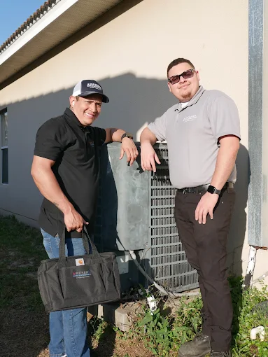Two technicians smiling next to outdoor residential unit