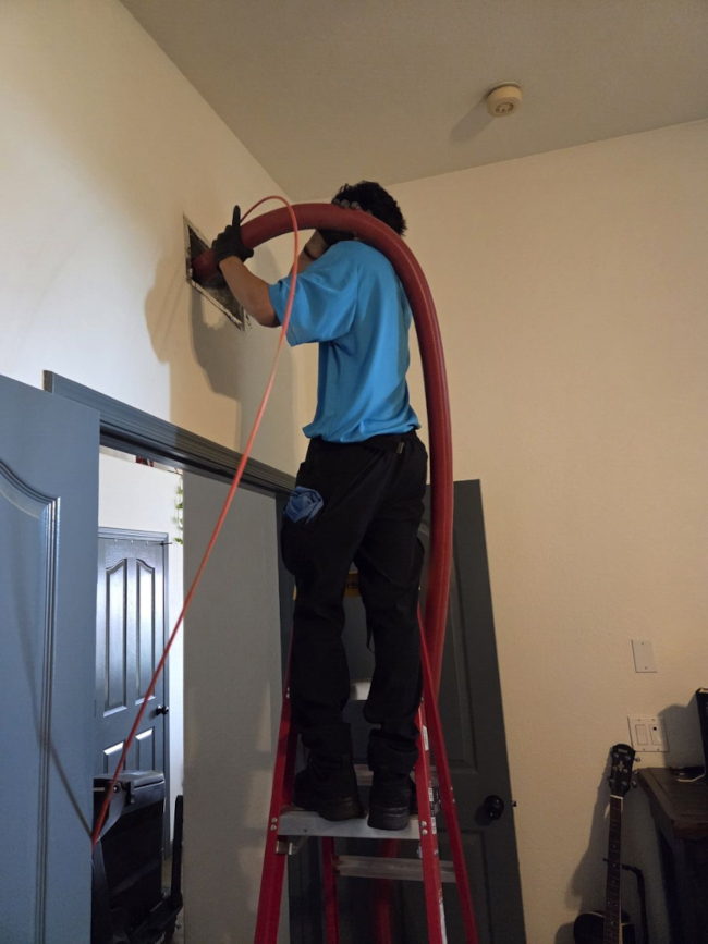 Aire Serv technician Victor on a ladder using professional Rotobrush equipment to clean ceiling air vents for a customer.