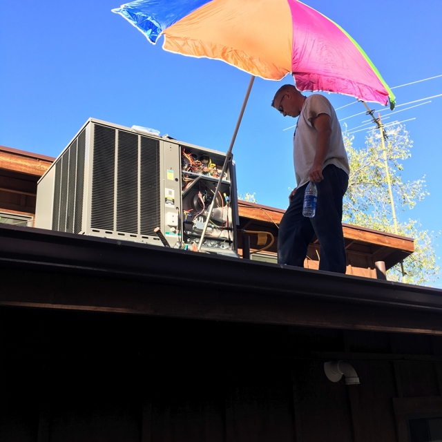 technician on roof next to ac unit under umbrella