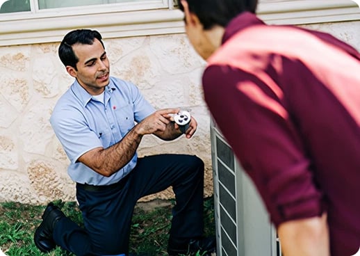 Aire Serv technician crouching beside outdoor HVAC unit explaining repairs to customer.