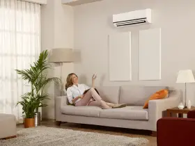 A woman uses a remote to control her mini split AC unit while sitting on the couch. | Aire Serv® of Western North Carolina