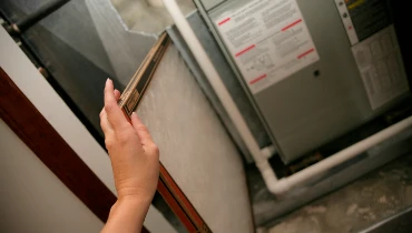 A female hand slides a new air filter into a furnace. | Aire Serv of {DBA}