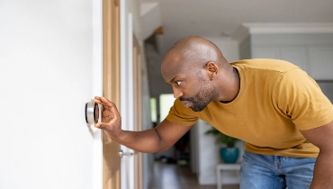 A man bends over to adjust a smart thermostat in his home. | Aire Serv of Jackson