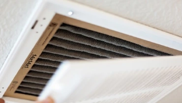 A person removes a vent cover revealing a dusty air filter. | Aire Serv of Western North Carolina