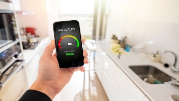 Person in kitchen at home viewing air quality index on mobile phone | Aire Serv