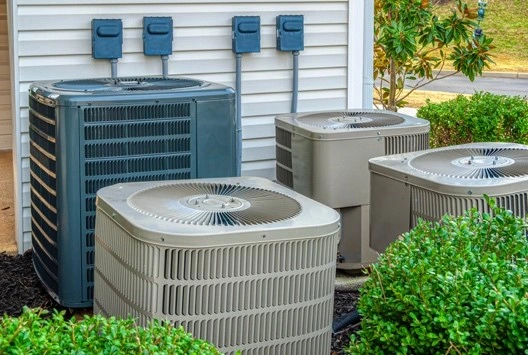 The outdoor condenser coils of four air conditioners are shown next to an apartment complex. | Aire Serv of Citrus County