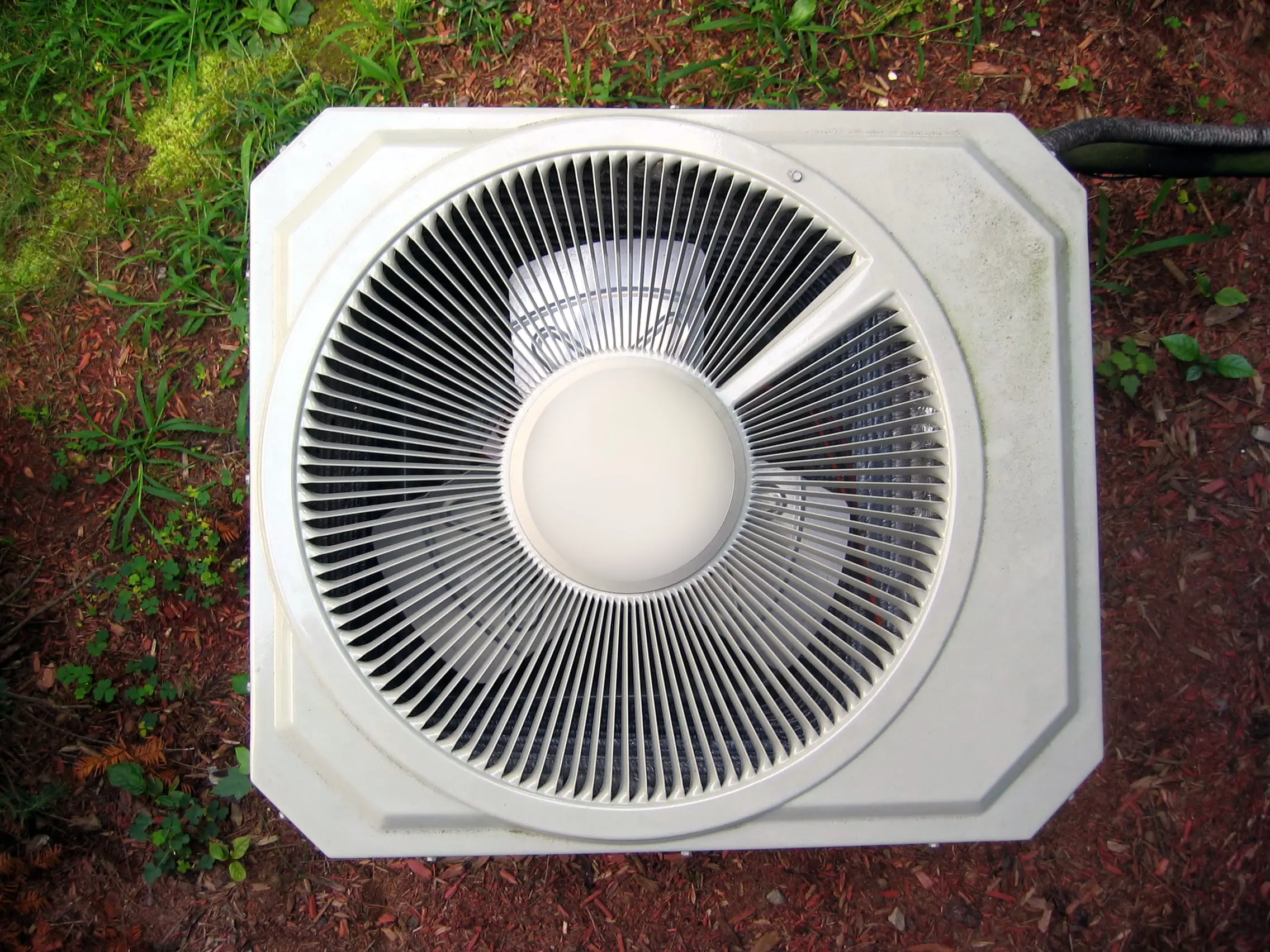 An aerial view of a central air conditioner installed in a yard next to a home. 