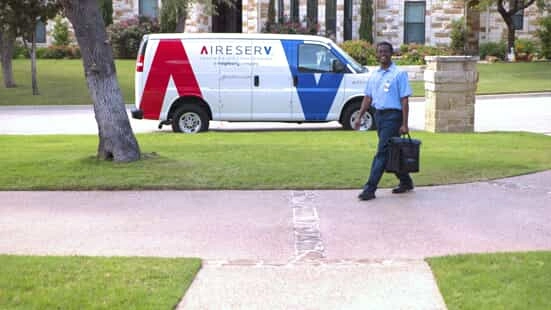 An HVAC service professional from Aire Serv walking from a work van toward a home in need of a new furnace.