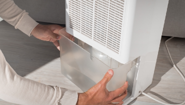 Person removing the water reservoir from a home dehumidifier