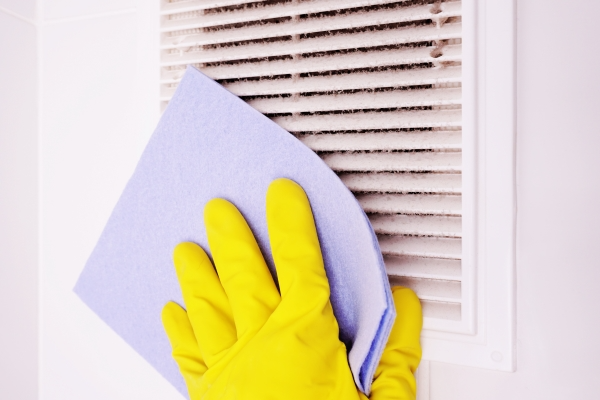 Person wearing yellow rubber gloves using a purple towel to clean a dirty air vent.