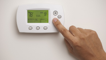Hand on digital thermostat set at 78 degrees