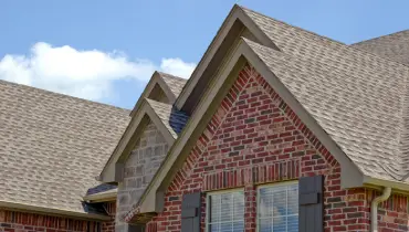 A close-up view of a modern brick house with a shingled roof on a sunny day. | Aire Serv® of Jackson