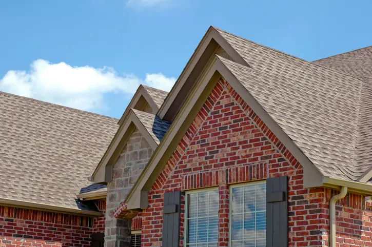 A close-up view of a modern brick house with a shingled roof on a sunny day. | Aire Serv® of Jackson