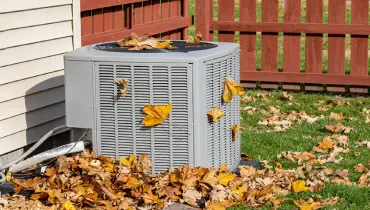 An outdoor condenser unit is covered in leaves during autumn. | Aire Serv of Western North Carolina