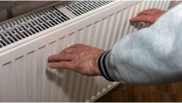 Man warming hands near a radiator in a home