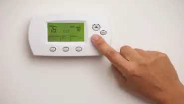 A close-up view of a person’s hand adjusting the temperature on a digital thermostat. | Aire Serv of North Central Arizona