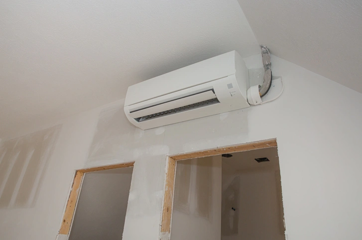 A white ductless mini split air conditioner at the top of a white wall.