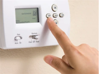 Person pushing button on digital thermostat