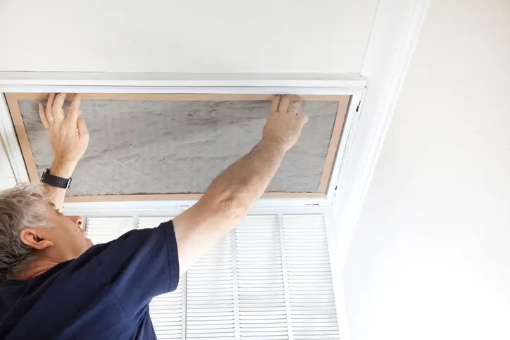 A man removes a dirty air filter from a vent in his home. | Aire Serv of Jackson