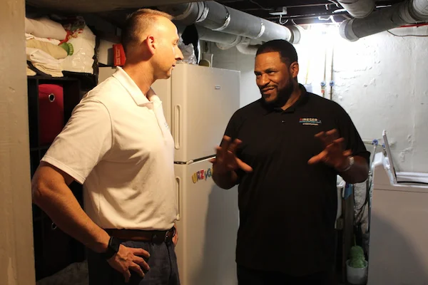 Jerome Bettis standing beside an Aire Serv service professional in residential basement.