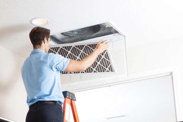 A man on a ladder removes an air filter from a vent. | Aire Serv of North Central Arizona
